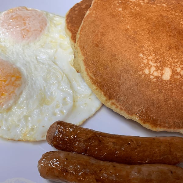 A diner breakfast with two fried eggs, two pancakes, and two sausage links on a white plate.