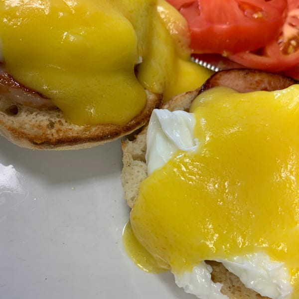 Eggs Benedict with bright yellow hollandaise sauce and sliced tomatoes on a white plate.