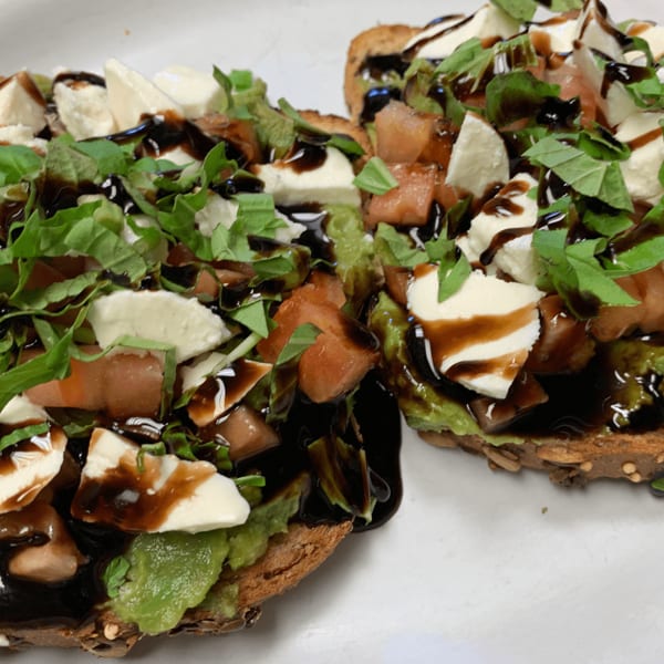 Two avocado toasts topped with mozzarella, diced tomatoes, basil, and balsamic glaze.