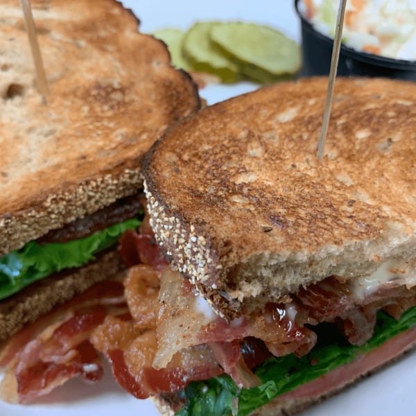 A Country Ham N' Eggs BLT sandwich with crispy bacon, lettuce, tomato, pickles, and coleslaw.